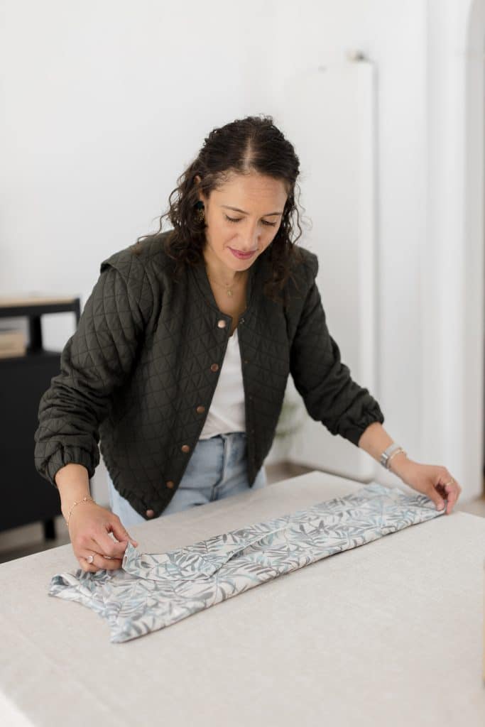 Femme pliant un linge à motif végétal sur une table claire, méthode de rangement optimisée.