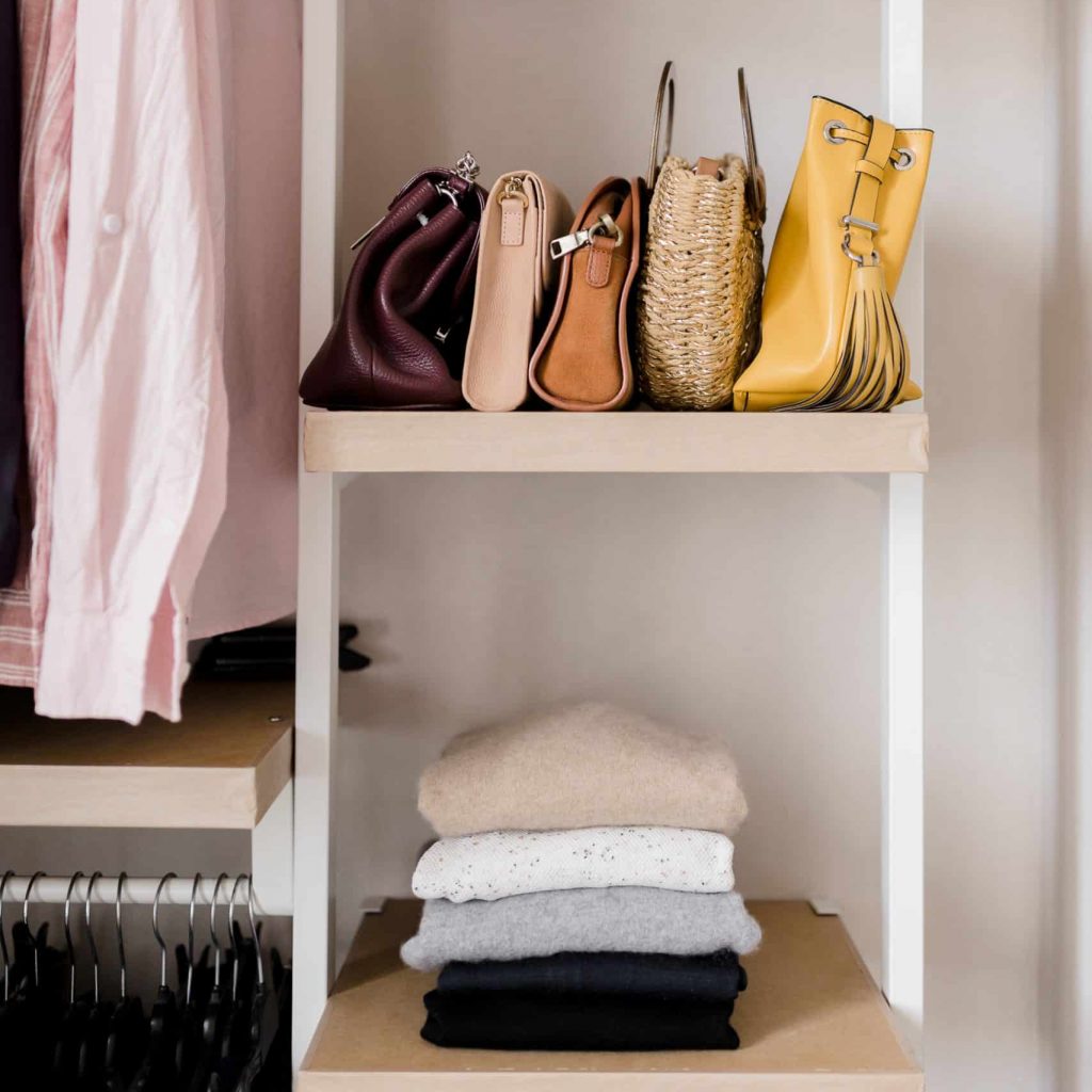 Étagères de dressing avec sacs, vêtements pliés et suspendus, dans un rangement ordonné et esthétique.