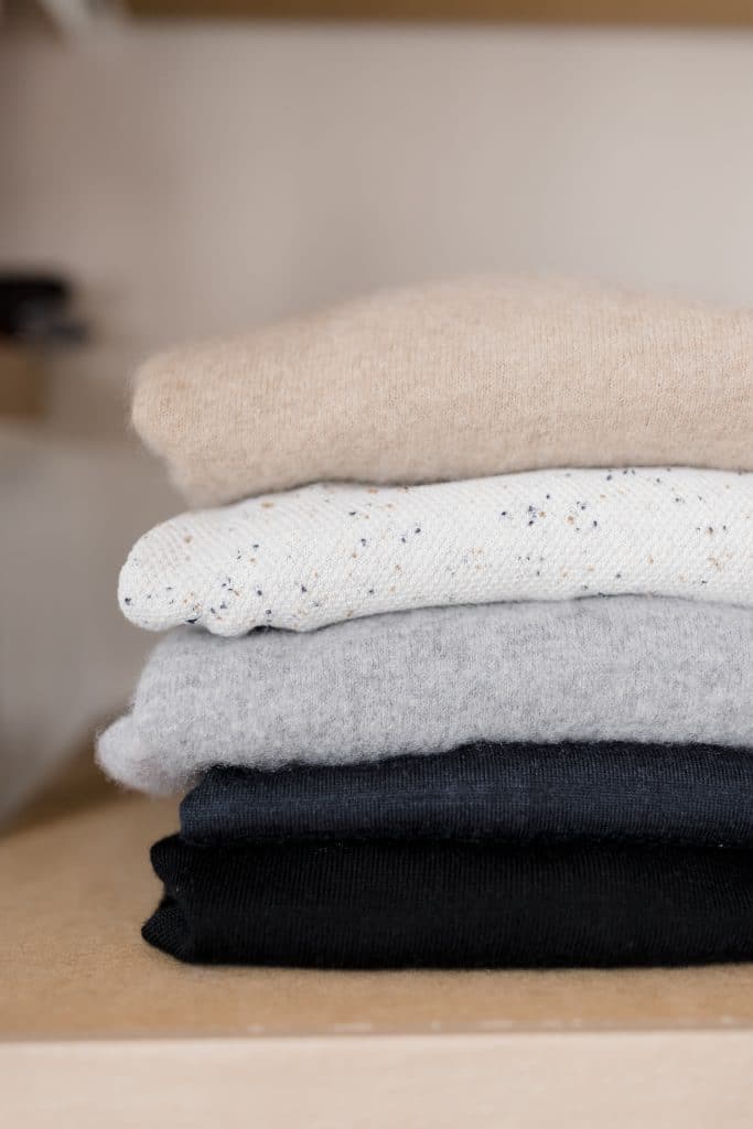 Pile de pulls pliés dans des tons neutres sur une étagère de dressing.