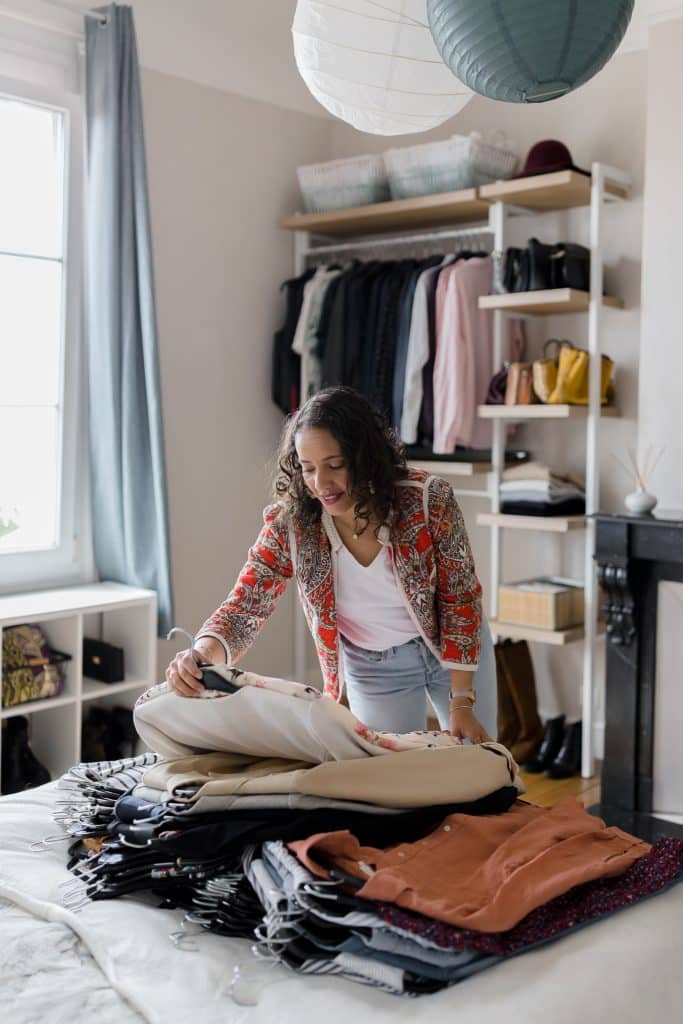 Audrey, home organiser à Reims, triant des vêtements sur un lit dans une chambre lumineuse.