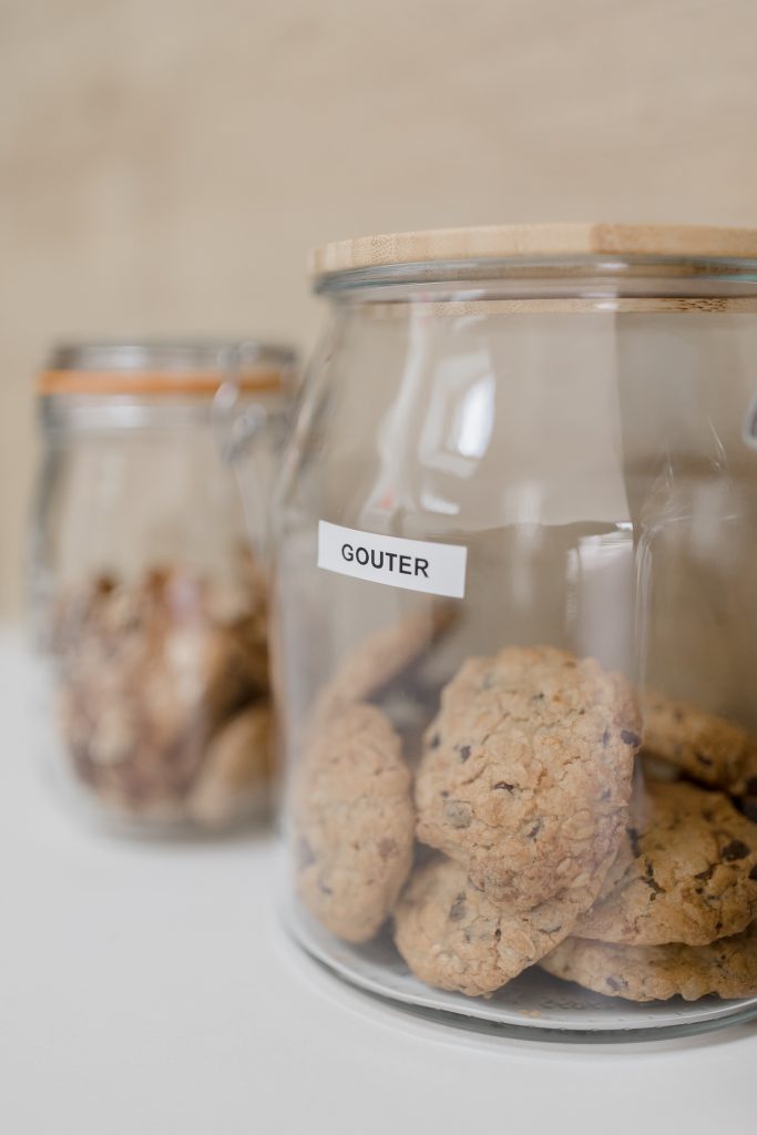 Deux bocaux en verre étiquetés “Goûter”, remplis de biscuits, illustrant une cuisine organisée et agréable à vivre.